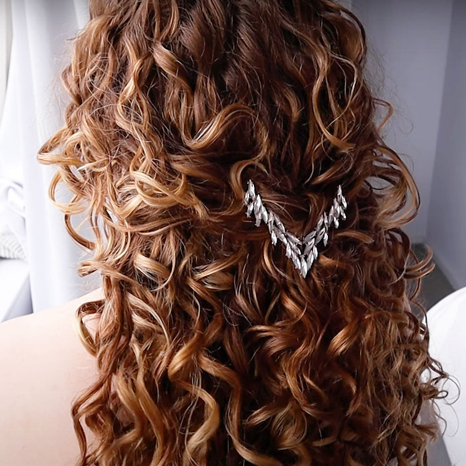 Person wearing a curly wedding hairstyle with voluminous brown curls and a silver leaf hair accessory