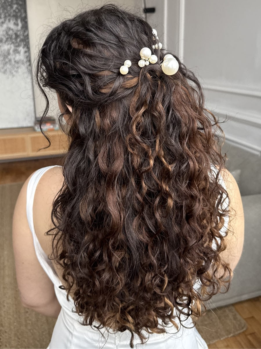 Back view of person wearing long dark curly hair extensions styled with pearl accessories for a wedding