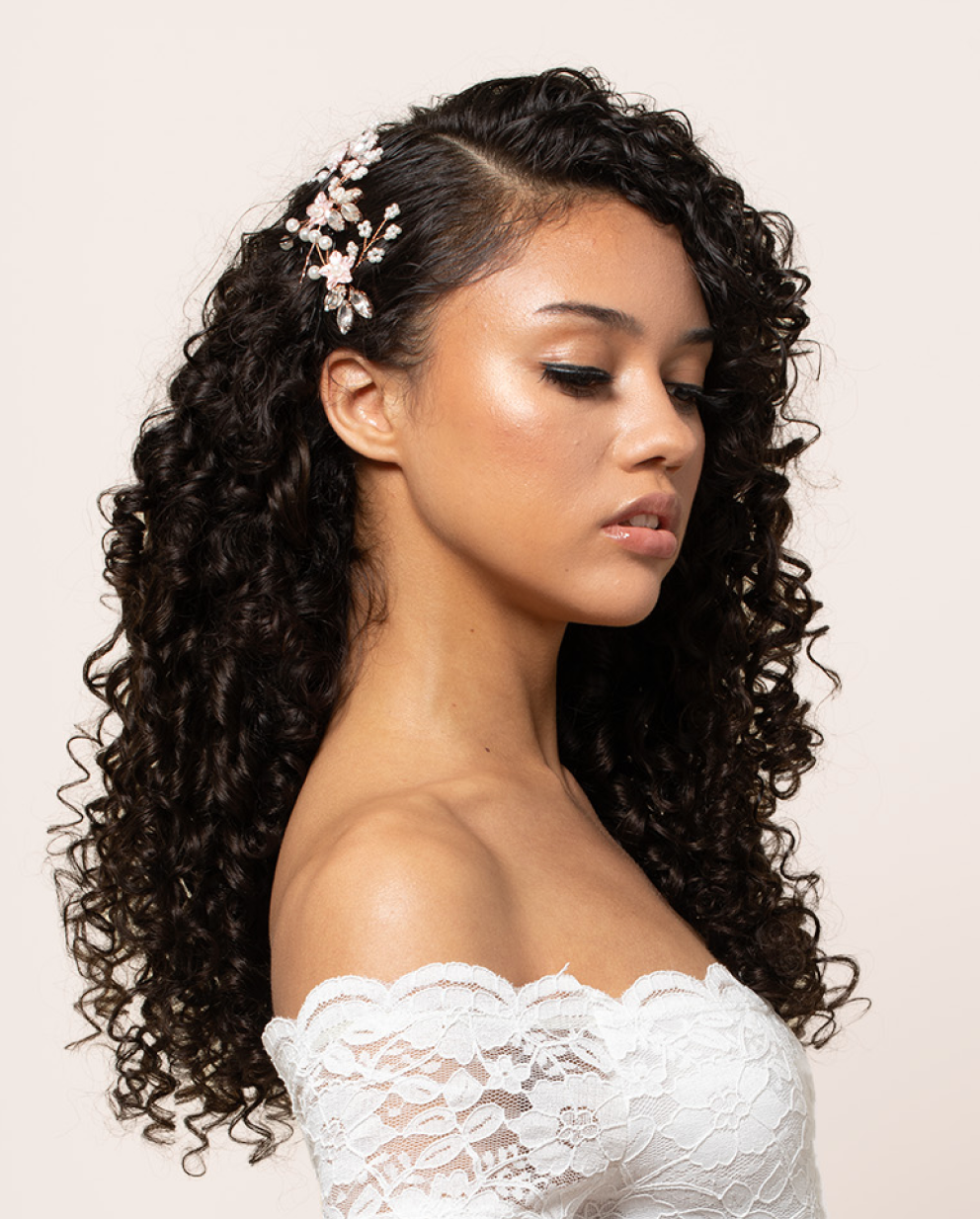 Model showcasing long dark curly bridal hairstyle with a floral hair accessory
