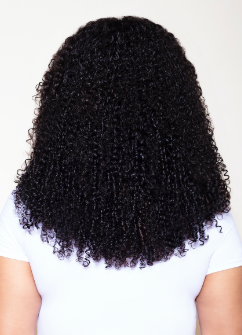 Back view of curly hair extensions showcasing upper chest-length curls on a person in a white shirt